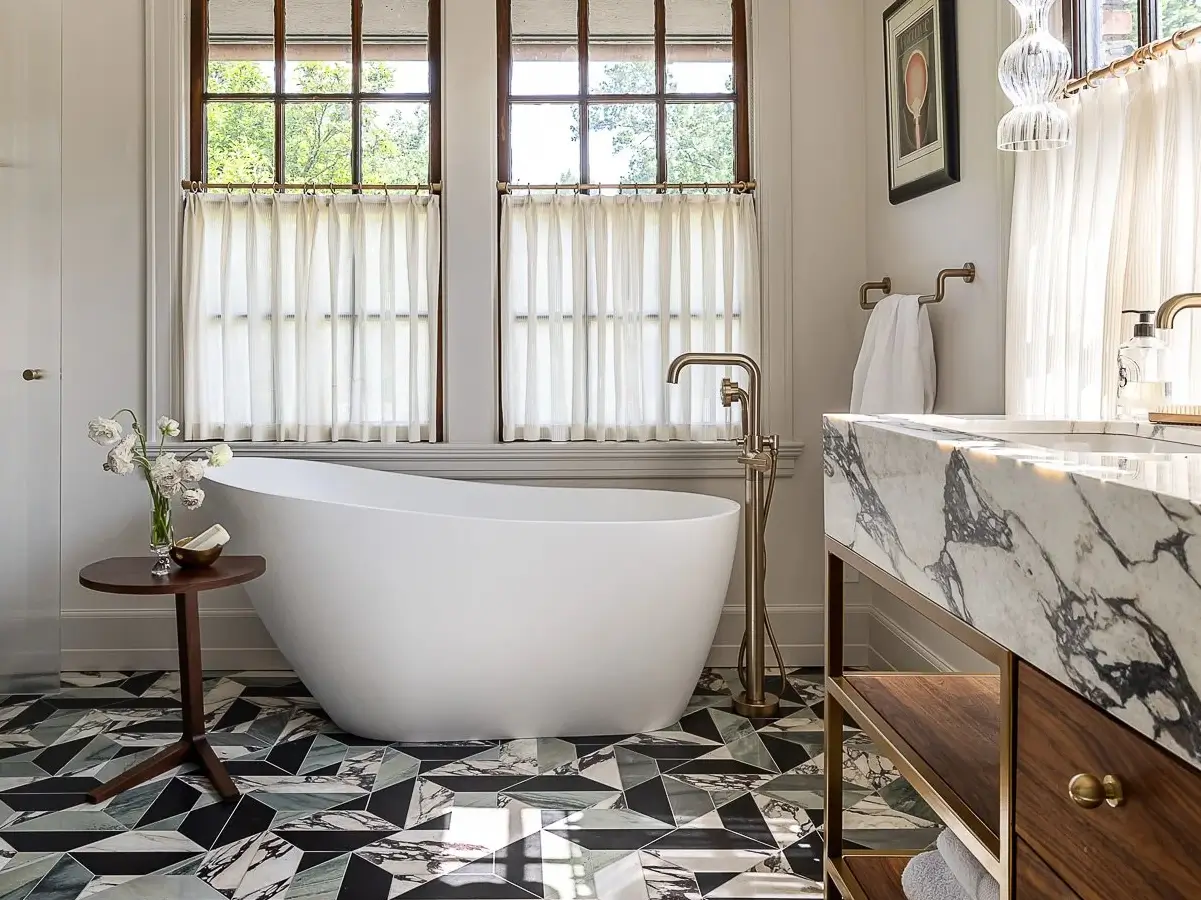 Modern bathroom with geometric marble mosaic floor tiles, freestanding bathtub, and marble vanity in warm neutral tones.