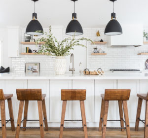 White Kitchen with black pendant lights, cognac leather bar stools, wood floors, open shelving