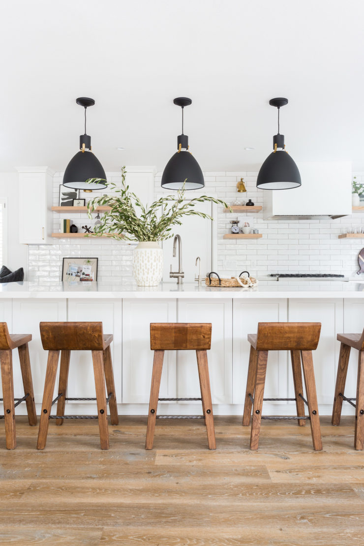 White Kitchen with black pendant lights, cognac leather bar stools, wood floors, open shelving