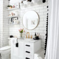 small black and white bathroom with round mirror and open shelves