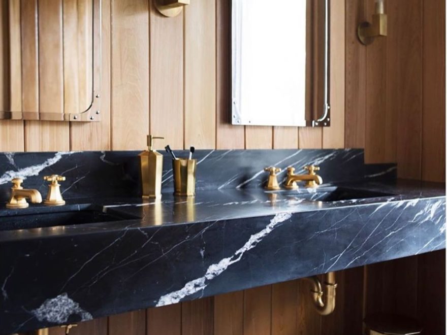 bathroom with luxury marble vanity and gold hardware wood paneling and black and white flooring