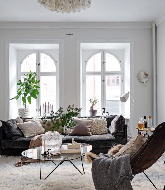bright Scandinavian living room with large windows white walls black sofa leather armchair and plants