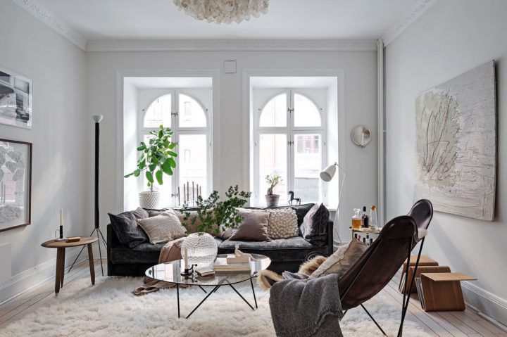 bright Scandinavian living room with large windows white walls black sofa leather armchair and plants 