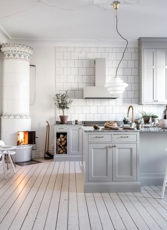 Scandinavian light grey and white kitchen with traditional swedish fireplace and white wood flooring