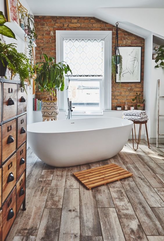 modernboho bathroom wiyh brick wall wood look flooring tiles free standing tub apothecary cabinet and indoor plants