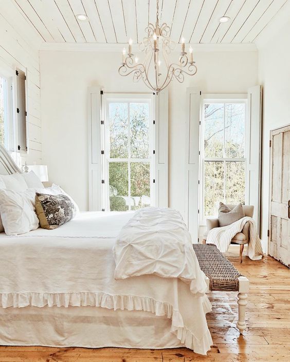 French Farmhouse Bedroom with shiplap ceiling, shutters, chandelier, and rustic wood floors 