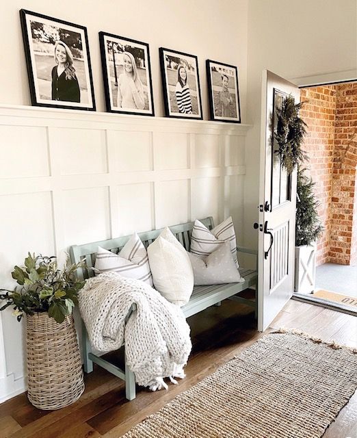 farmhouse style entryway with bench with pillows and blanket and black and white family photographs wall decor