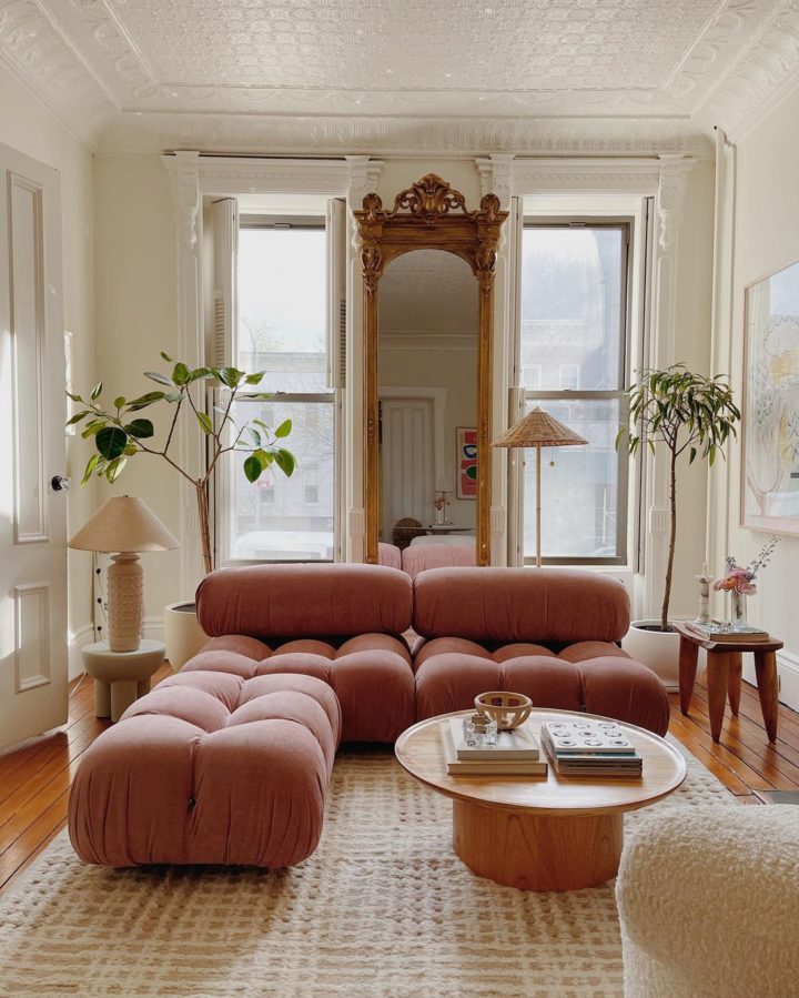 living room with pink modular sofa  gold floor to ceiling wall mirror and rounf wood coffee table