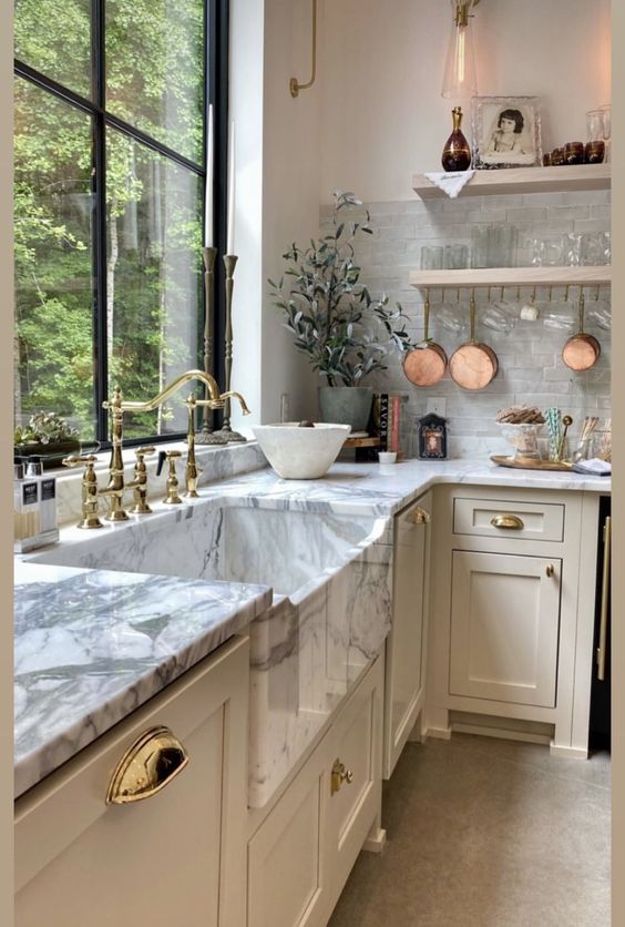 cream kitchen with white marble counter floating shelves large window above the marble sink and floating shelving