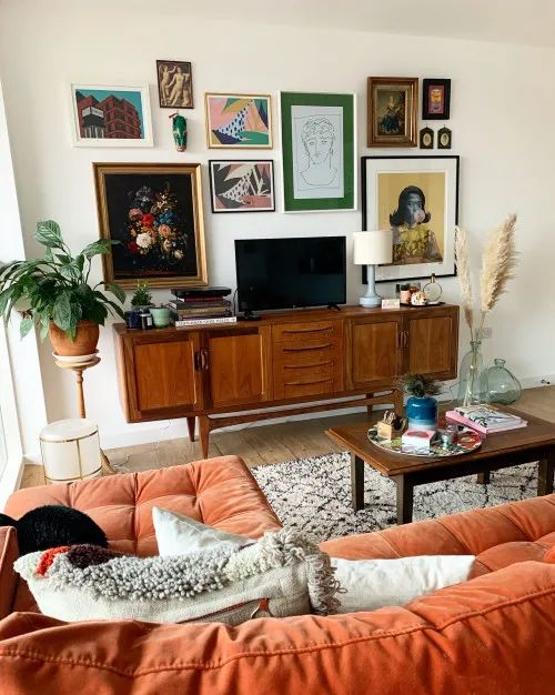 small mid century modern living room with orange sectional sofa and gallery wall above TV vintage sideboard