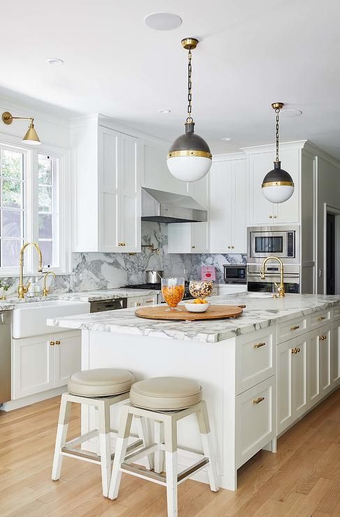 white shaker kitchen island donning antique brass pulls and a white and gray honed marble countertop
