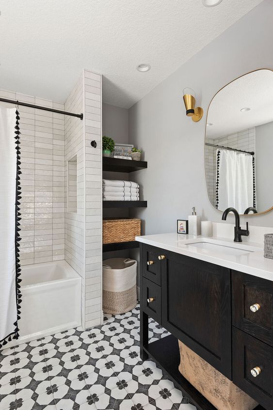 b;ack and white bathroom with patterned floor, a tonal white tile ark rich cabinet finish and  mix of black and gold hardware