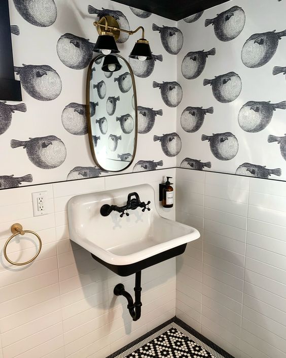 Bathroom with white tiles,black and white wallpaper and brass and black sconces
