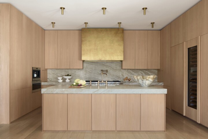 open-concept Scandinavian design kitchen with white oak cabinets and custom brass hood