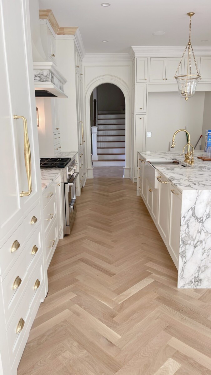 white elegant kitchen with white callacatta marble island and herringbone wood floor pattern