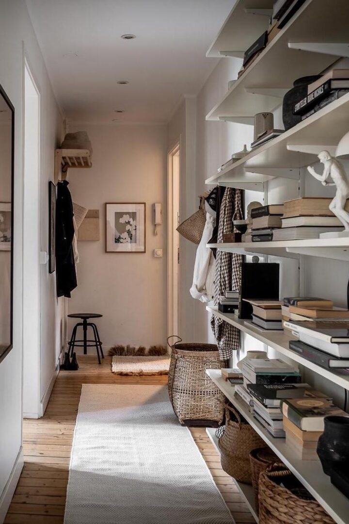 Scandinavian narrow hallway with IKEA BOAXEL open sheving storage system that stretches from floor to ceiling, a neat modern coat rack along with a simple wooden mail sorter, black IKEA KULLABERG stool, an ivory rug runner