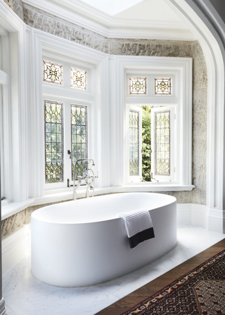 bathroom with contempporary freestanding tab in front of a wall of convict-worked sandstone and stained-glass windows by Hancock Architects