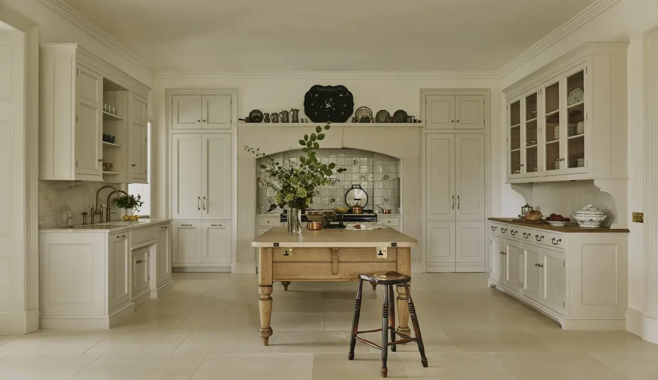 Traditional cream-colored kitchen with shaker cabinets, a wooden island, stone countertops, and a decorative tiled backsplash framed by an elegant arched range alcove.