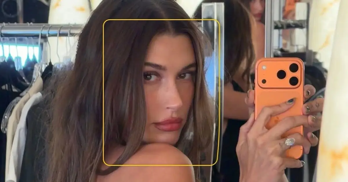 Hailey Bieber takes a mirror selfie in a strapless black dress, showing off her long brunette hair and minimal beauty look.