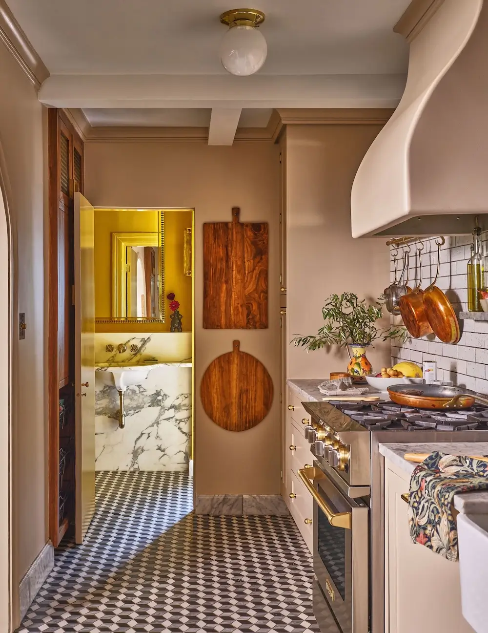 Warm cinematic galley kitchen with geometric floor tiles, sculptural plaster range hood, hanging copper cookware, marble surfaces, wood cutting boards, brass hardware, and soft golden lighting inspired by European apartment interiors.