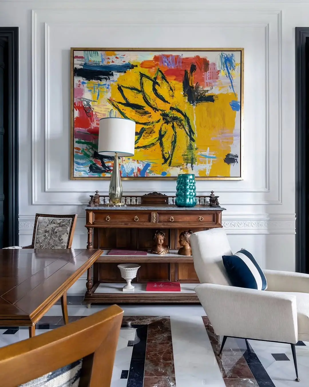 Dining area in a restored Murcia mansion with classic wooden sideboard, large colorful abstract painting, marble geometric flooring, and a mix of traditional and modern furniture.