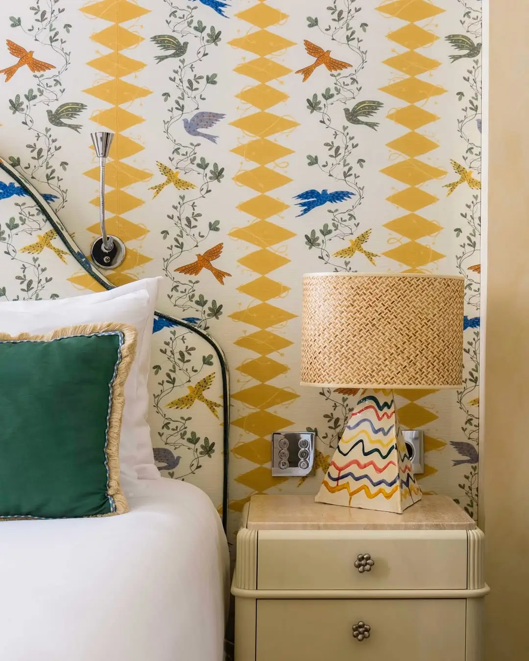 Bedroom corner inside the Michael McGregor Art Suite at Casa Monti Rome featuring illustrated bird-pattern wallpaper, colorful ceramic lamp, and layered boutique hotel interiors inspired by Roman motifs.