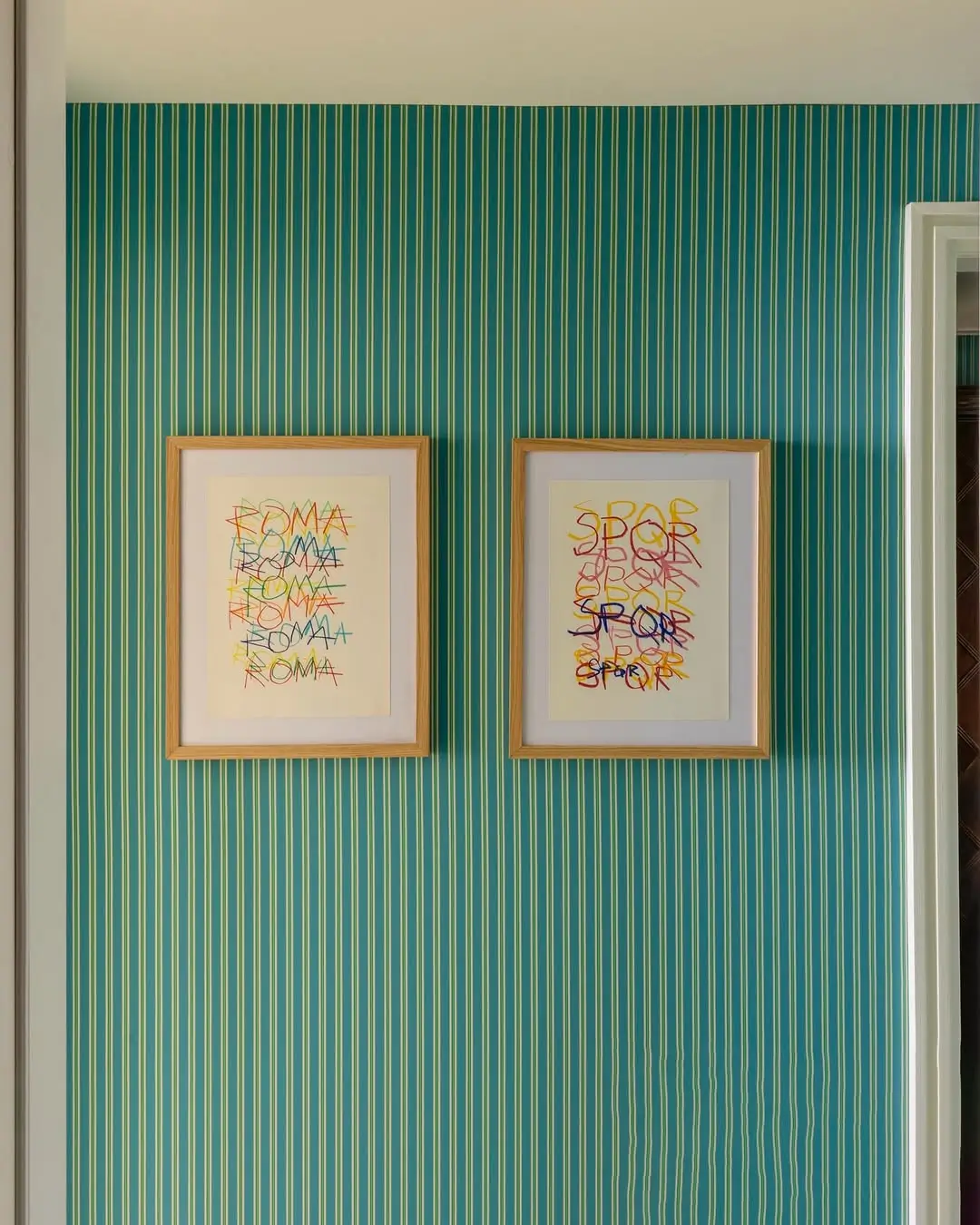 Framed “Roma Amor” artworks displayed against striped teal wallpaper inside the Michael McGregor Art Suite at Casa Monti Rome.
