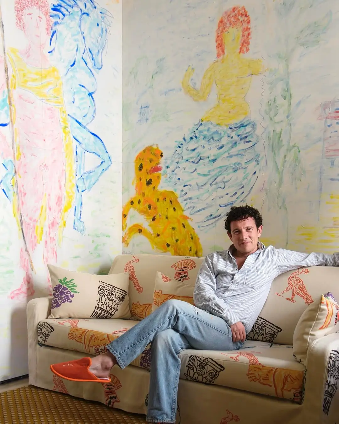 Artist Michael McGregor sitting inside his immersive art suite at Casa Monti Rome, surrounded by pastel murals, illustrated textiles, and hand-drawn Roman-inspired interiors in his signature expressive style.