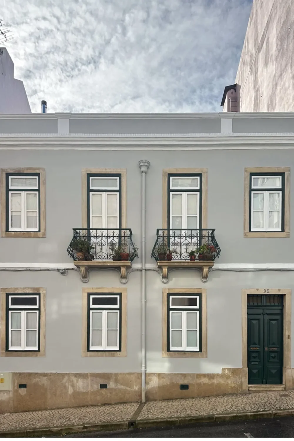 Traditional Portuguese townhouse with a pale gray facade, black-trimmed windows, wrought-iron balconies, and classic stone detailing.