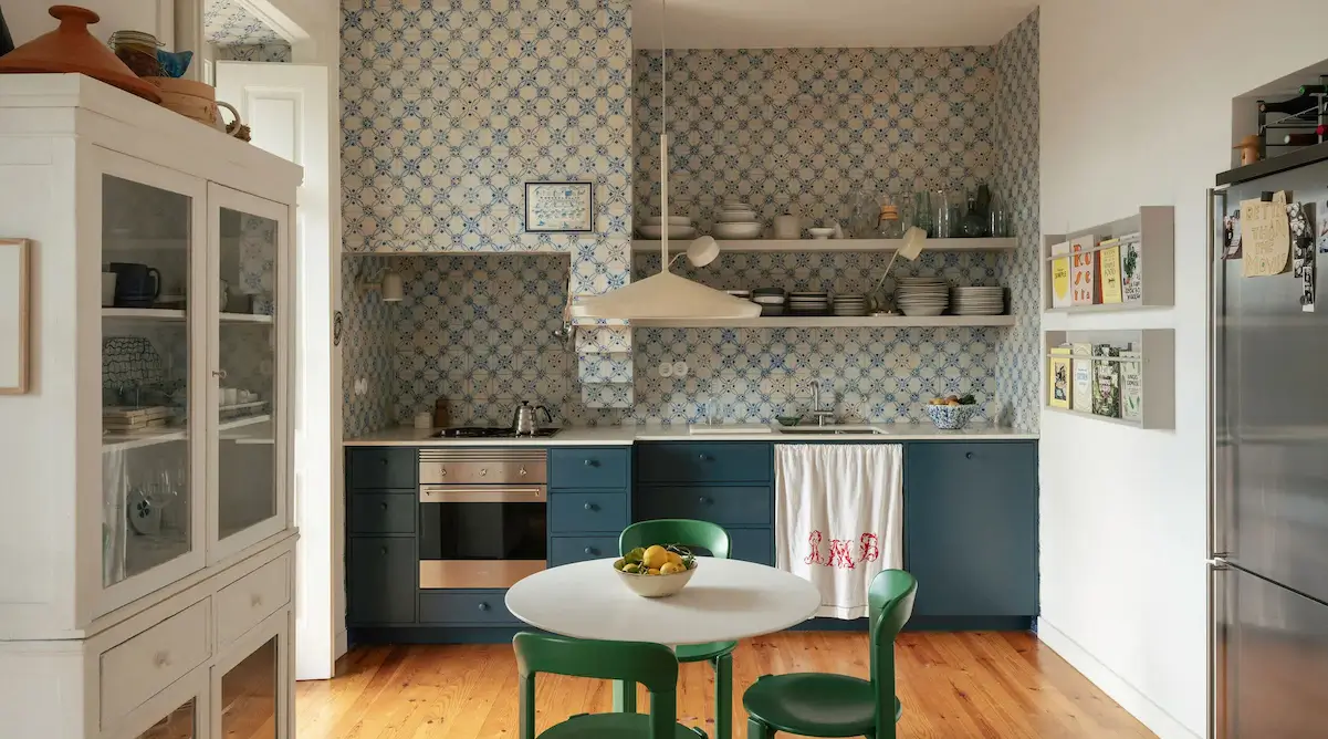 Traditional Portuguese kitchen with blue-and-white azulejo tile walls, deep blue cabinetry, open shelving, a white pedestal dining table, and green dining chairs in a renovated Lisbon townhouse.