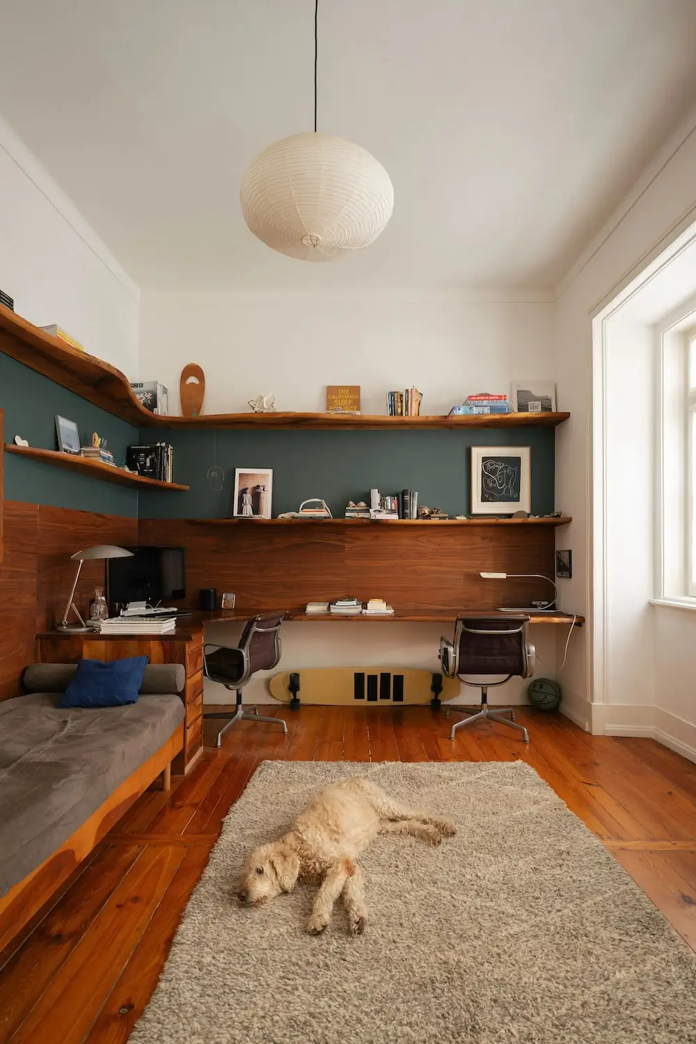 Custom walnut home office with built-in shelving, dual workstations, a daybed, warm wood floors, and a dog resting on a cream rug in a Lisbon townhouse.