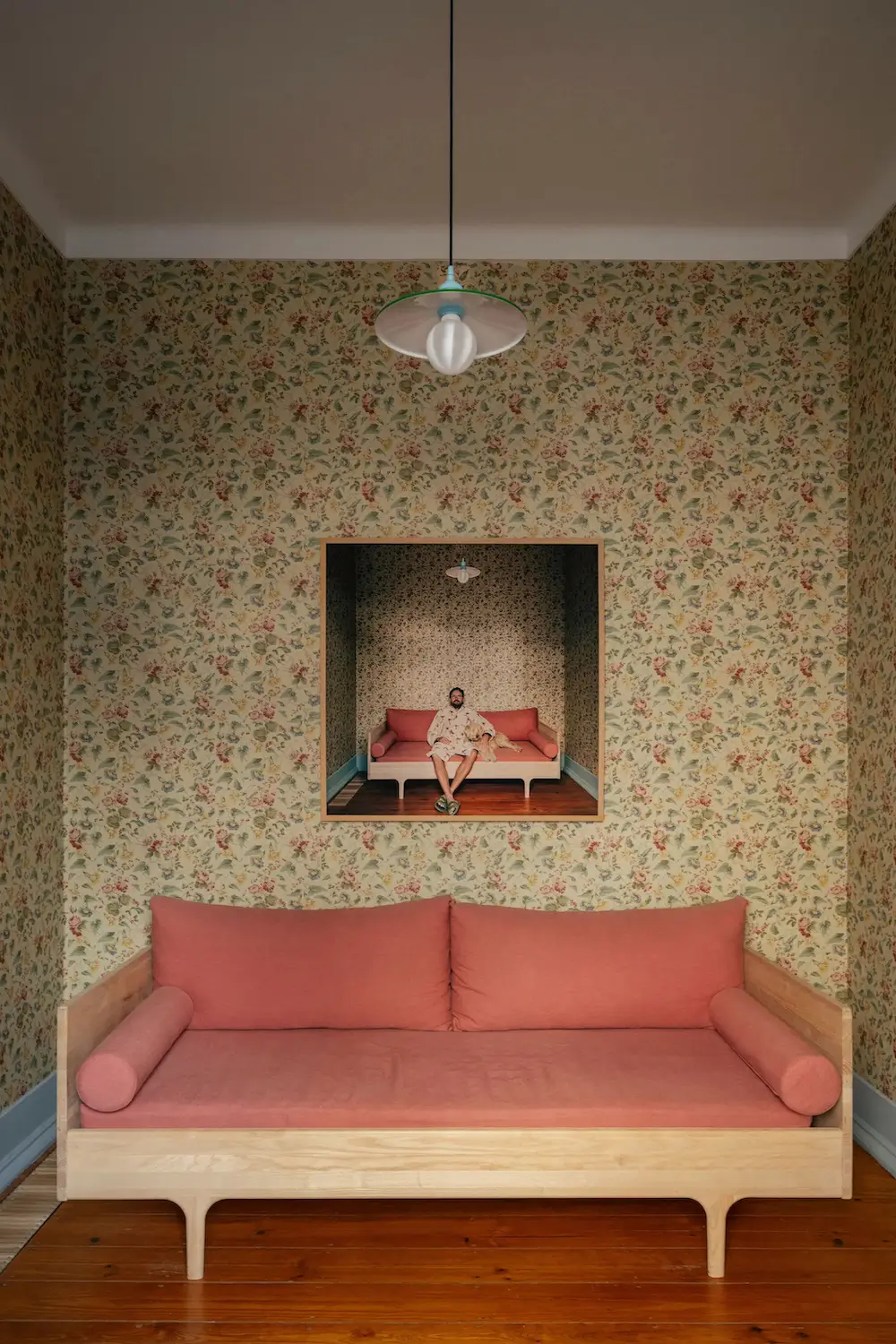Guest room with preserved floral wallpaper, a pink upholstered daybed, vintage-inspired lighting, and warm wood floors in a renovated Portuguese townhouse.