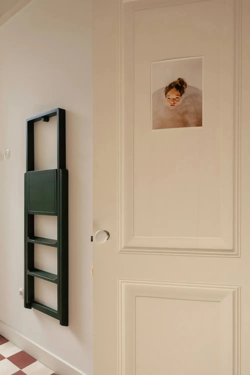 Traditional paneled door featuring framed artwork, checkerboard floor tiles, and a wall-mounted storage unit in a renovated Portuguese townhouse.