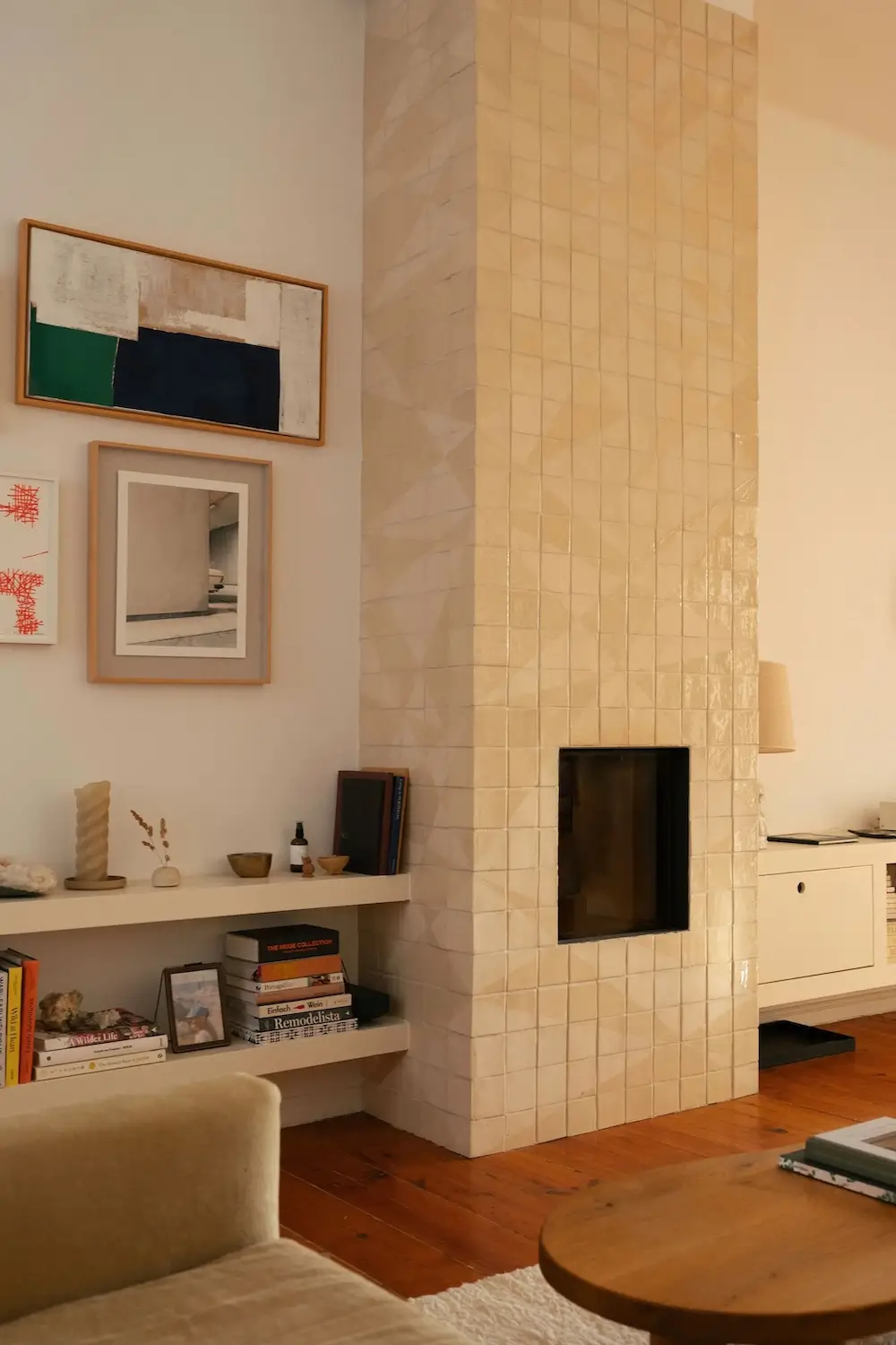 Custom fireplace clad in handmade Portuguese tiles surrounded by built-in shelves, books, artwork, and minimalist furnishings in a Lisbon townhouse.
