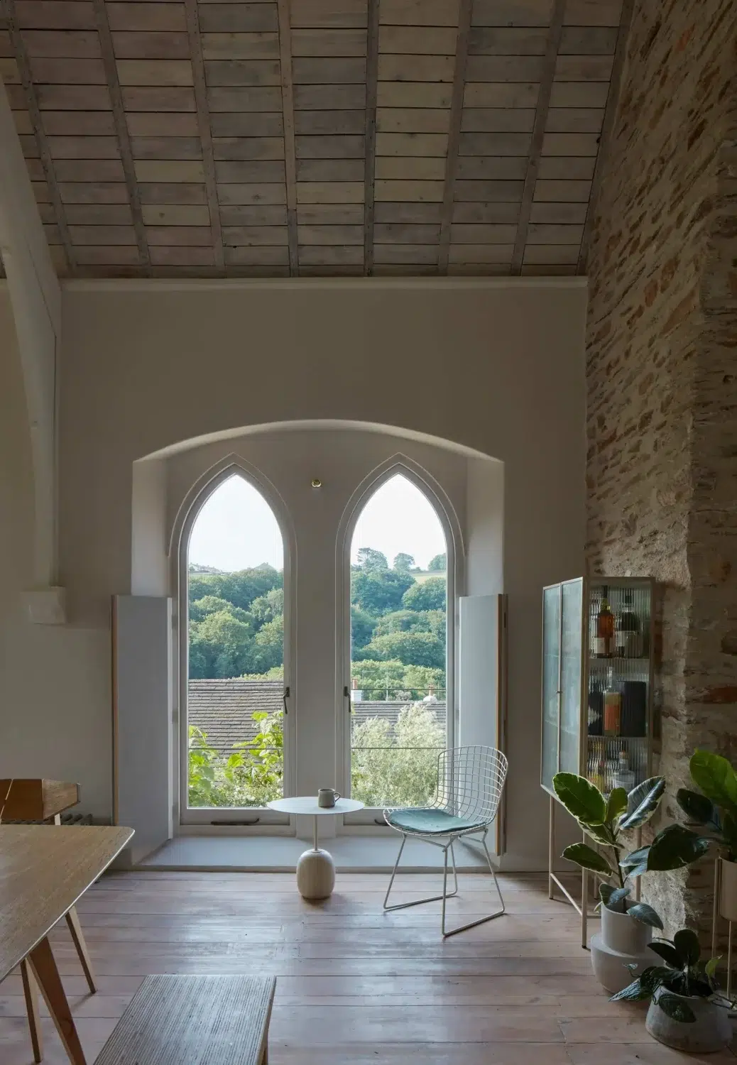 Seating area beside tall Gothic-style chapel windows overlooking the Devon countryside.