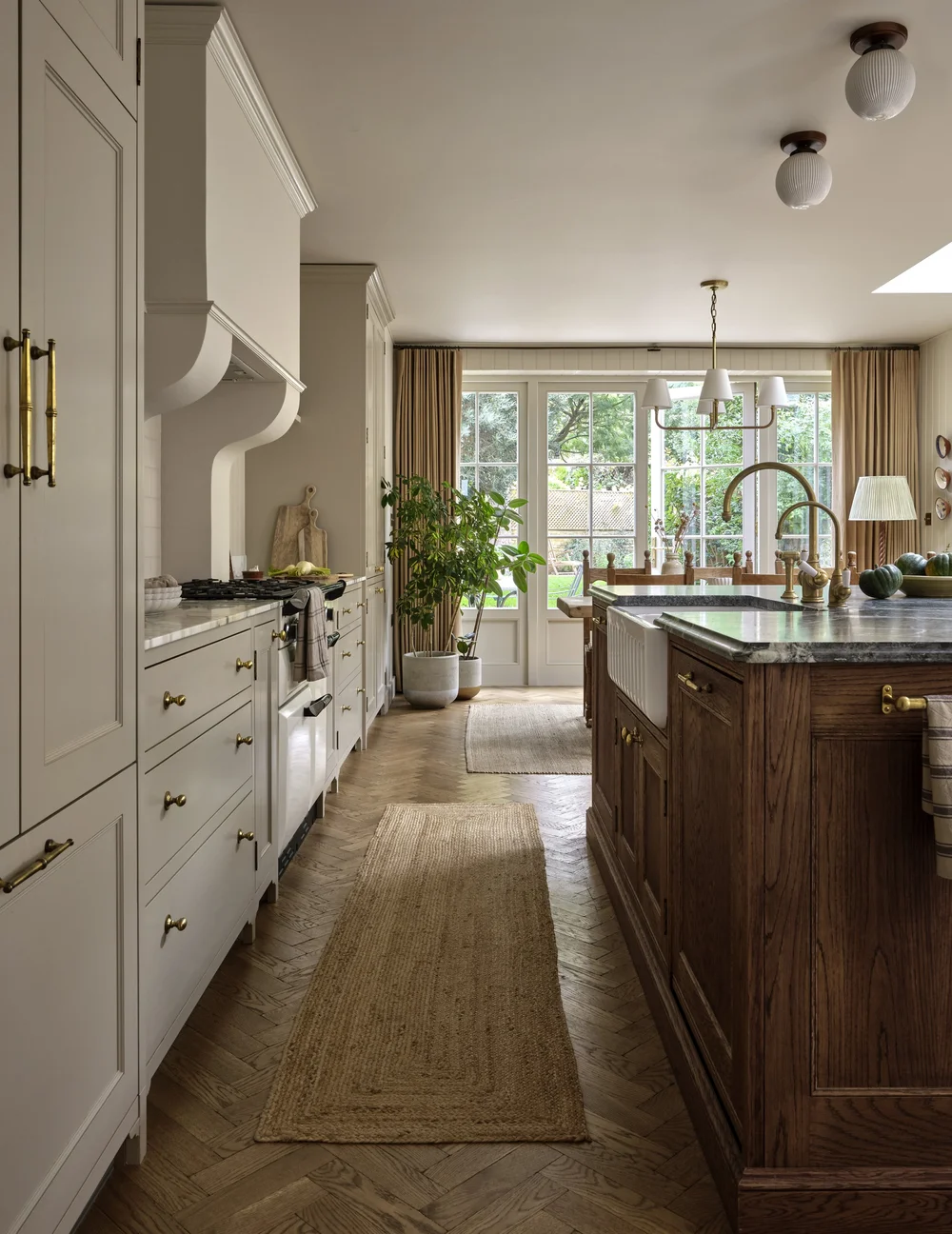 Galley kitchen in a renovated Victorian townhouse by Frank and Faber with warm shaker cabinetry, a dark oak island, brass fixtures, herringbone wood floors, and French doors opening to the garden.