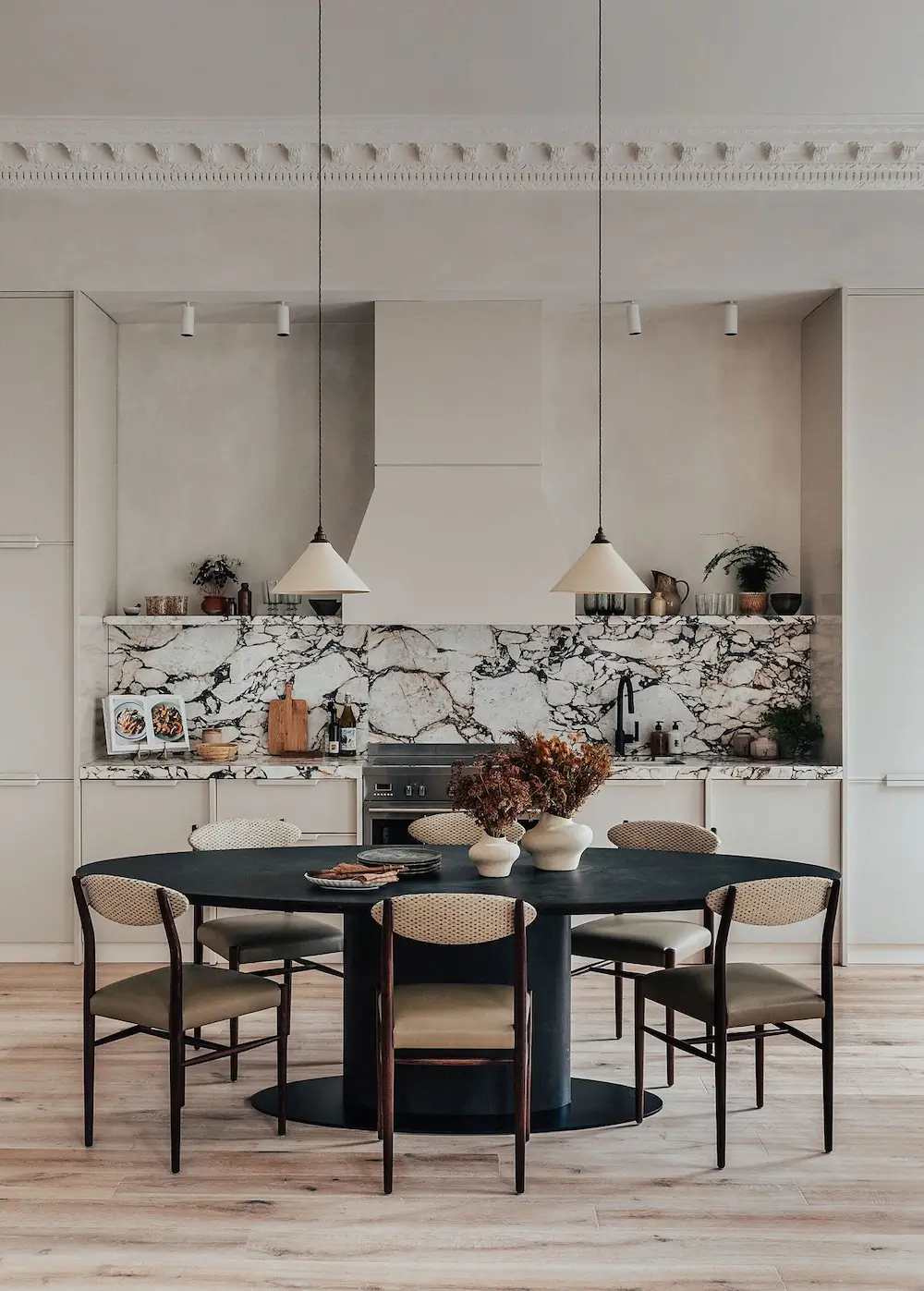 Contemporary kitchen with dramatic marble backsplash, cream cabinetry, and black oval dining table in a Mayfair apartment.