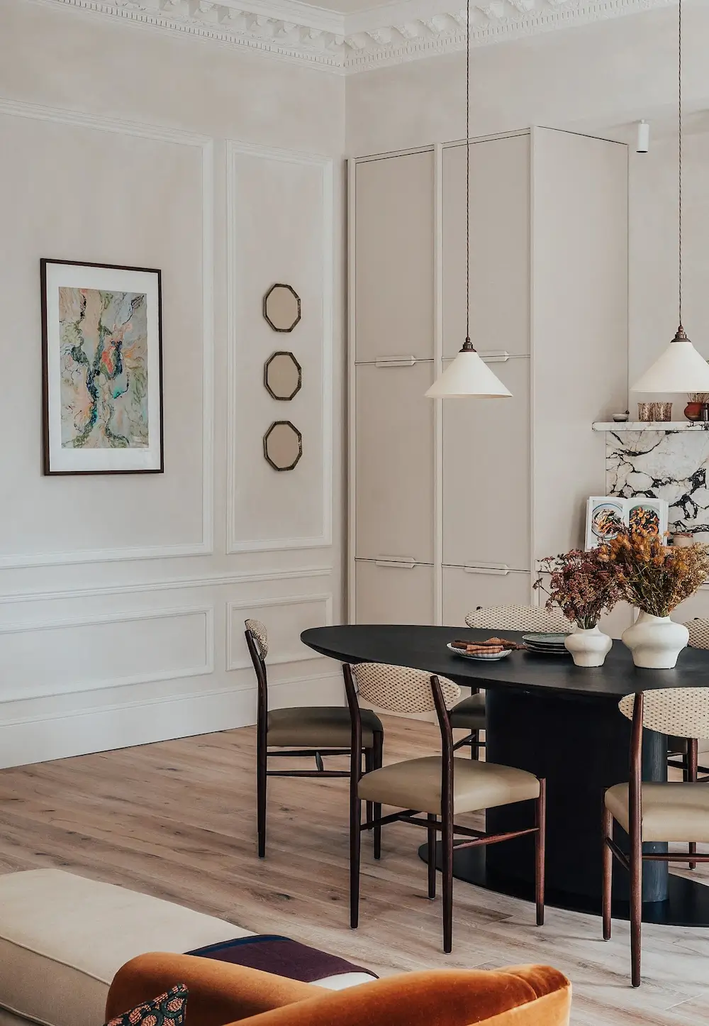Elegant dining area with black oval table, woven chairs, and classic wall paneling in a luxury London apartment.