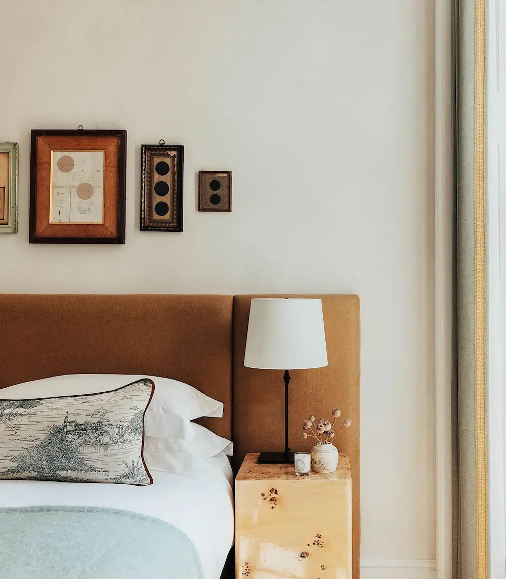 Warm neutral bedroom with upholstered headboard, burl wood bedside table, and vintage artwork in a Mayfair apartment.