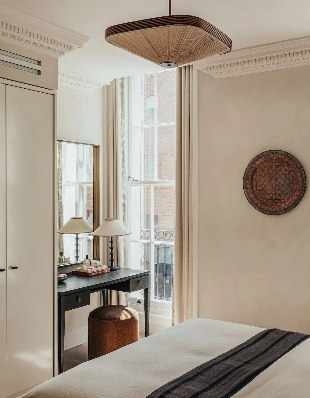 Bedroom dressing area with built-in desk, velvet stool, and tall sash window in a Mayfair pied-à-terre.