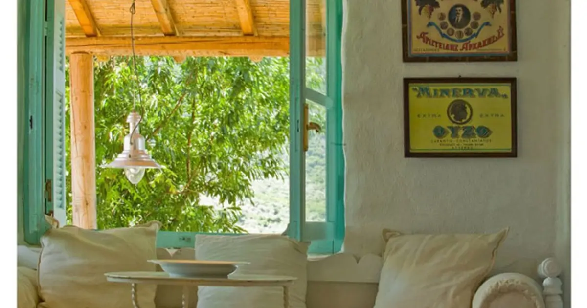 Traditional Greek island living room with mint green window frames, built-in seating and views of the lush Mediterranean landscape.
