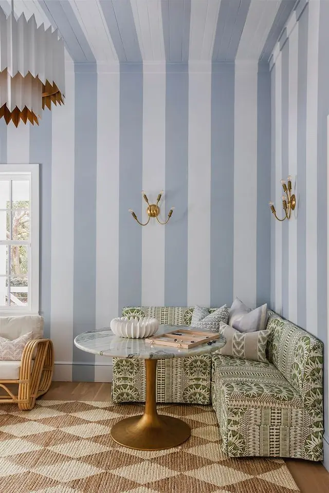 Coastal breakfast nook by Megan Molten Interiors featuring light blue striped wallpaper, a built-in banquette, and soft natural textures.