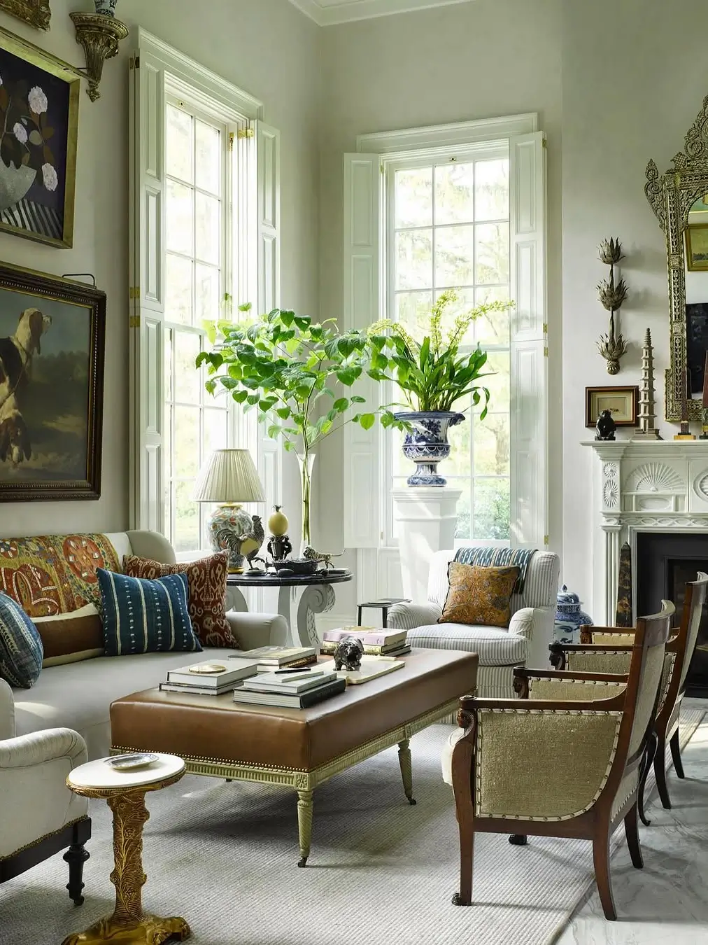 Sophisticated sitting room designed by Williams Lawrence featuring tall shuttered windows, antique furnishings, layered textiles, collected artwork, and lush indoor greenery.