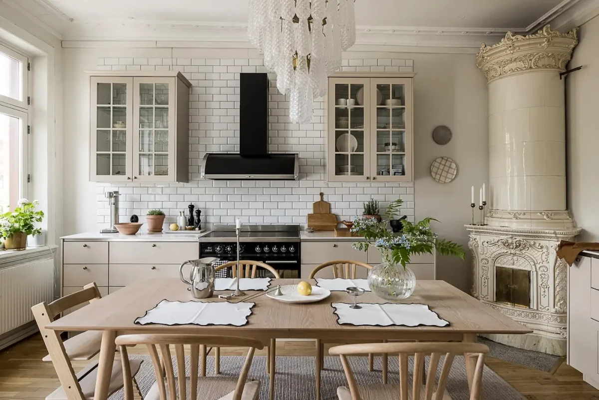 Scandinavian kitchen with cream cabinets, white subway tile backsplash, oak dining table, and an ornate ceramic tile stove.