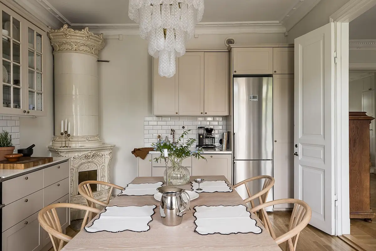 Scandinavian kitchen with cream cabinets, oak dining table, ornate ceramic tile stove, and white subway tile backsplash.