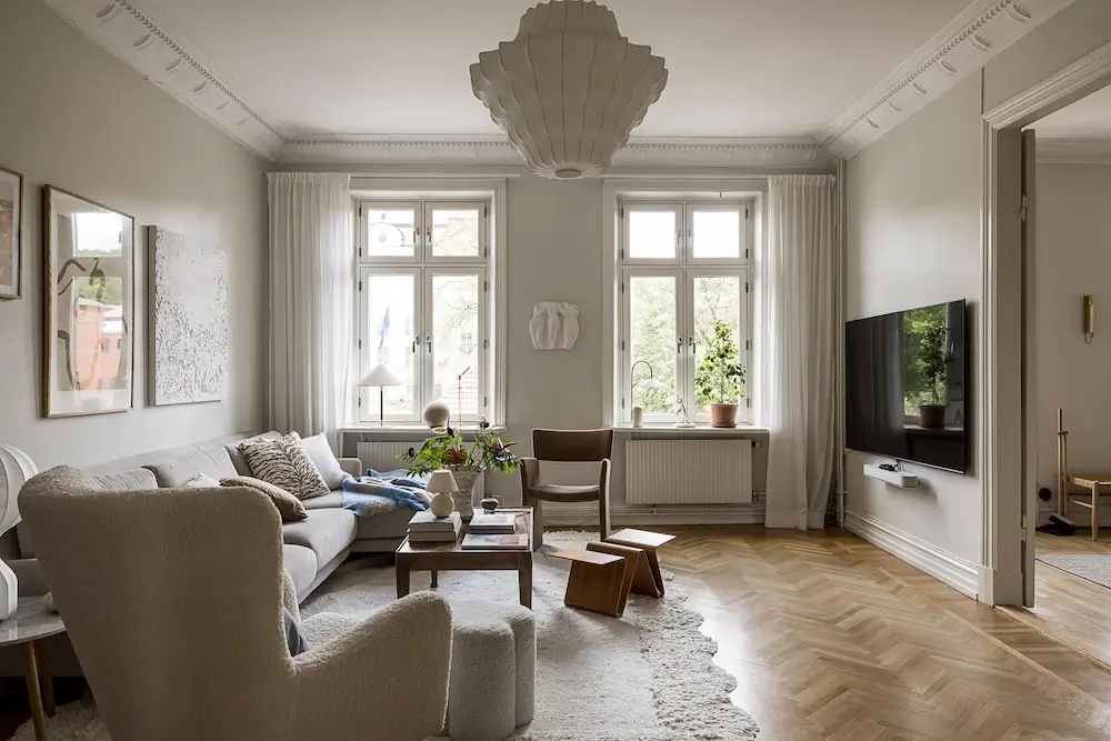 Neutral Scandinavian living room with soft furnishings, herringbone floors, and tall windows.