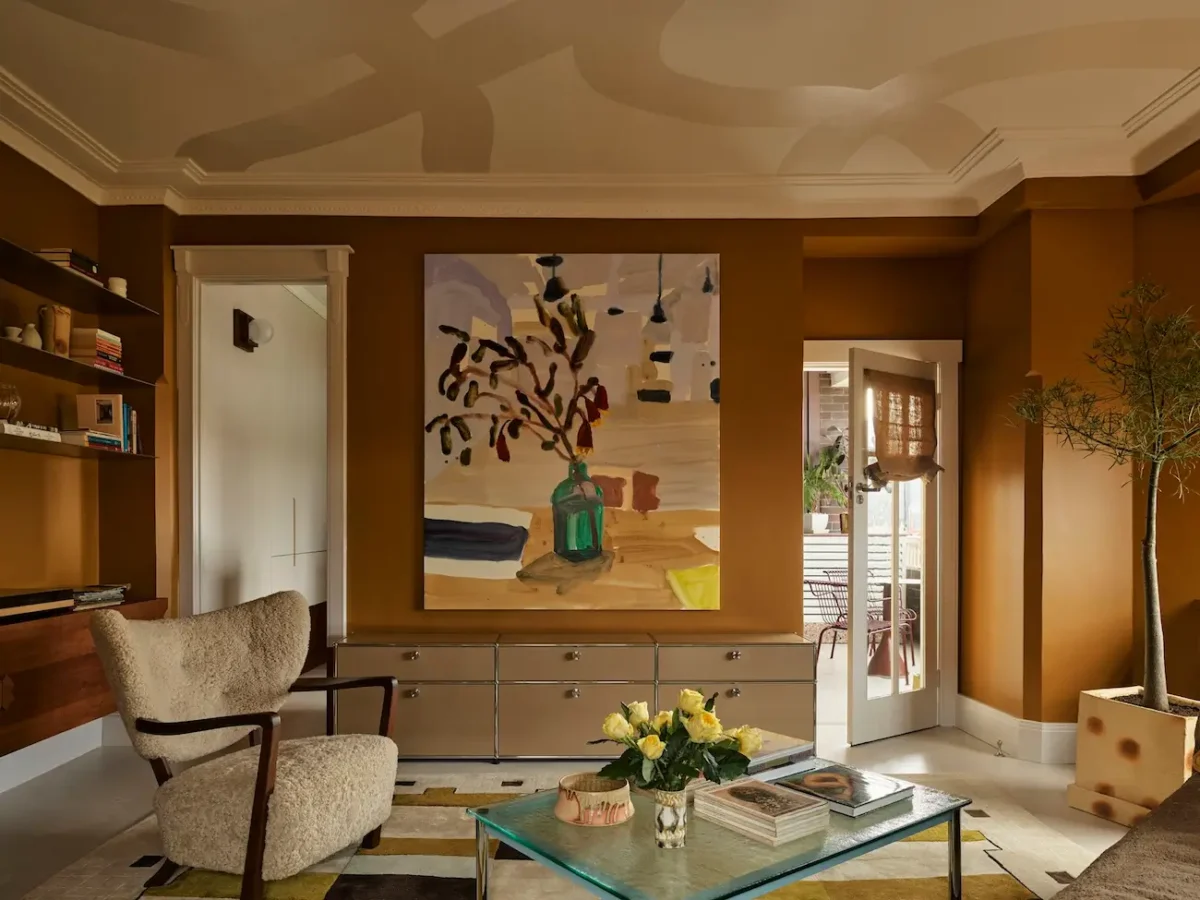 Warm Art Deco living room in The Gentleman apartment by YSG Studio with caramel walls, sculptural painted ceiling, polished aluminium sideboard, and abstract artwork.