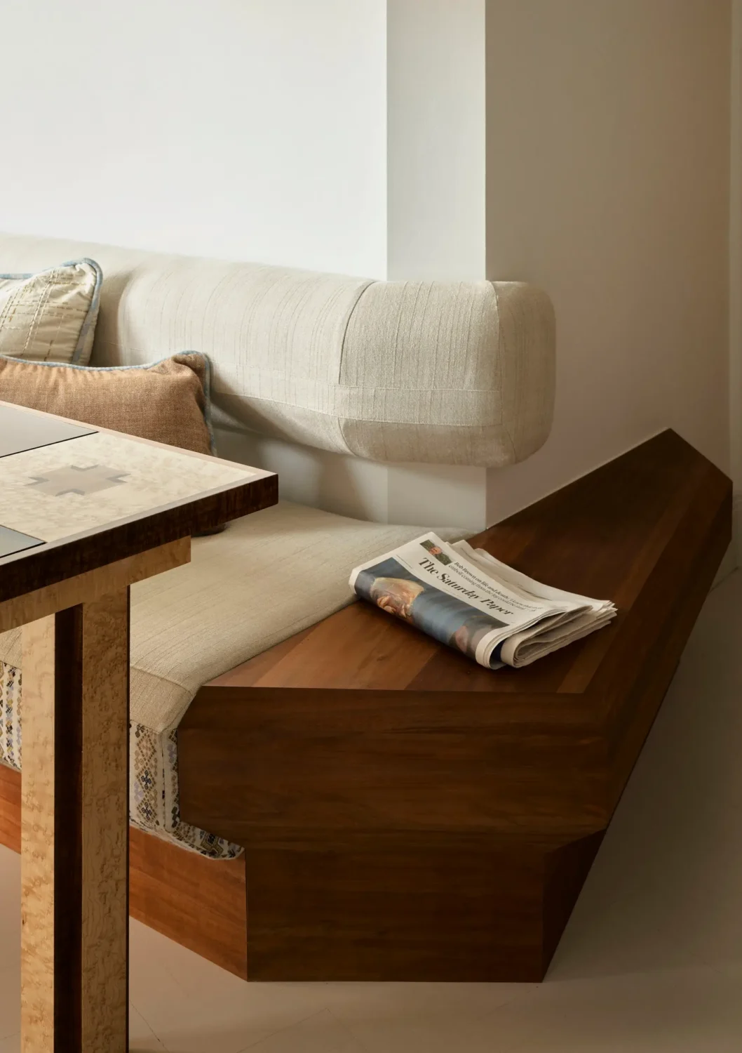 Custom walnut banquette with upholstered linen cushions in The Gentleman apartment by YSG Studio beside a bespoke dining table.