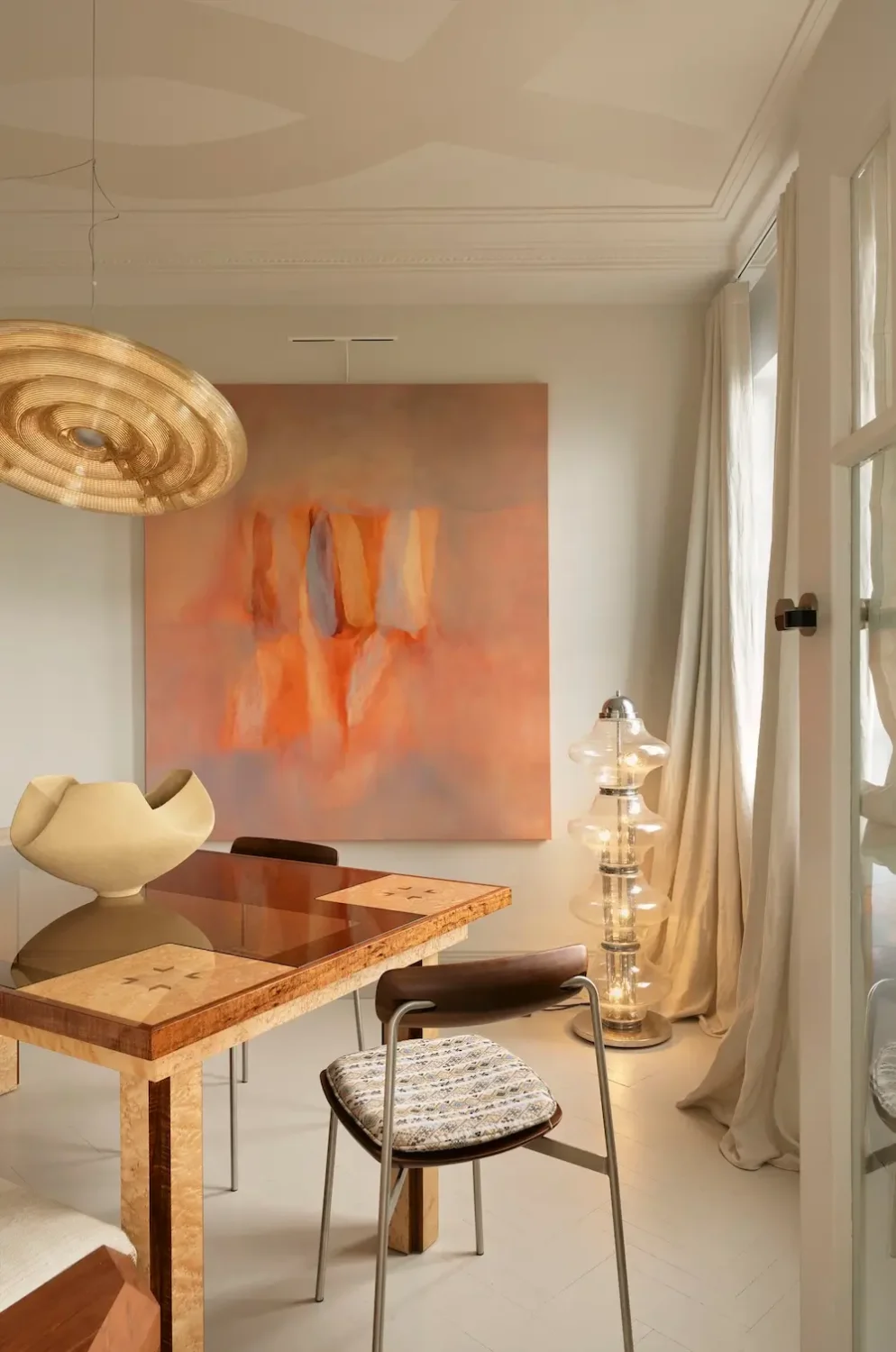 Elegant dining room in The Gentleman apartment by YSG Studio featuring a bespoke timber table, sculptural pendant light, abstract artwork, and flowing linen curtains.