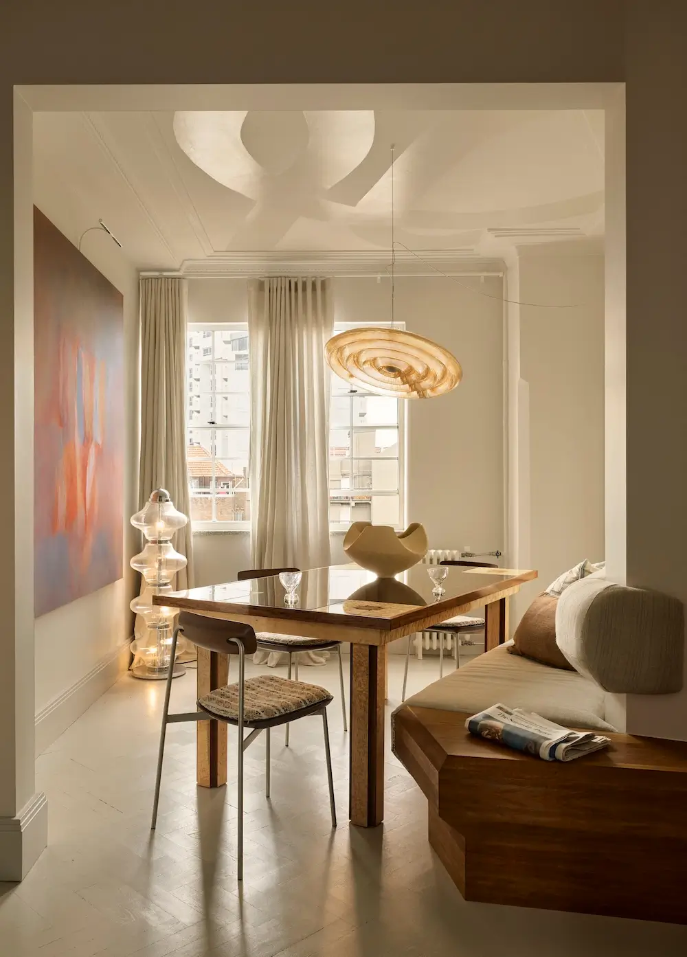 Custom timber banquette and bespoke dining table in The Gentleman apartment by YSG Studio with sculptural pendant light, linen curtains, and painted Art Deco ceiling.